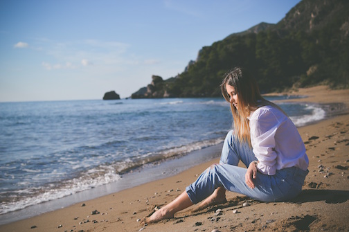 Woman sitting on a beach with her toes in the sand. 